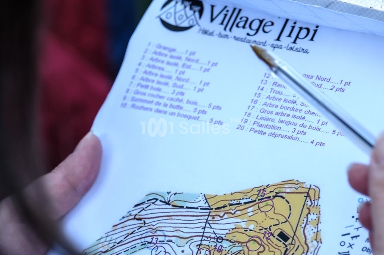 Une personne tient une carte et une liste d'indices pour une activité d'orientation dans un lieu nommé ’Village tipi’.