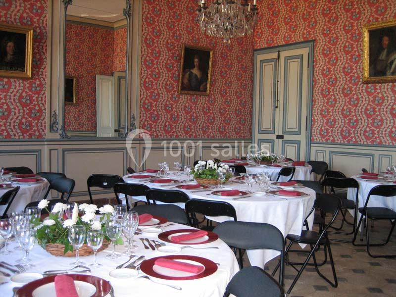 Salle de réception élégante avec tables rondes dressées, nappes blanches, serviettes rouges et décorations florales.