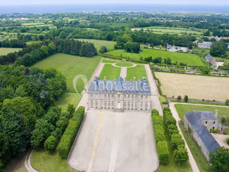 Vue aérienne d'un château entouré de jardins, d'allées gravillonnées et de vastes espaces verts en campagne.