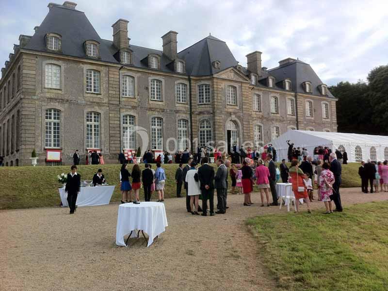 Groupe de personnes rassemblées devant un château en pierre, avec des tables dressées pour un événement en plein air.