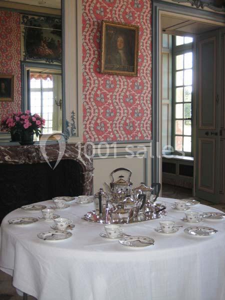 Table dressée pour le thé avec un service en argent, dans une pièce décorée de boiseries et de papier peint rouge à motifs.
