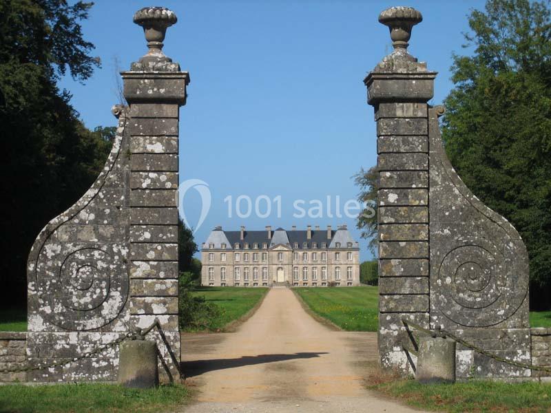 Portail en pierre ouvrant sur une allée bordée de pelouse menant à un château à l'architecture classique.