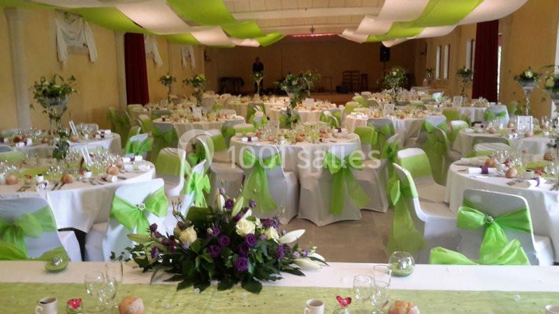 Salle de réception décorée avec des nappes blanches, des nœuds verts et des compositions florales sur les tables.