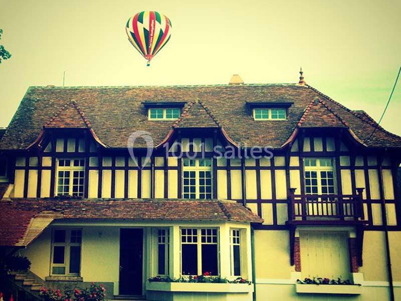 Montgolfière colorée flottant dans le ciel au-dessus d'une maison à colombages avec toit en tuiles.