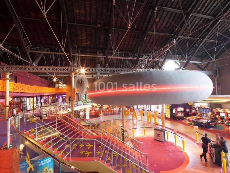 Intérieur d'un cinéma avec escalier, décorations colorées, enseigne lumineuse et espace de jeux.