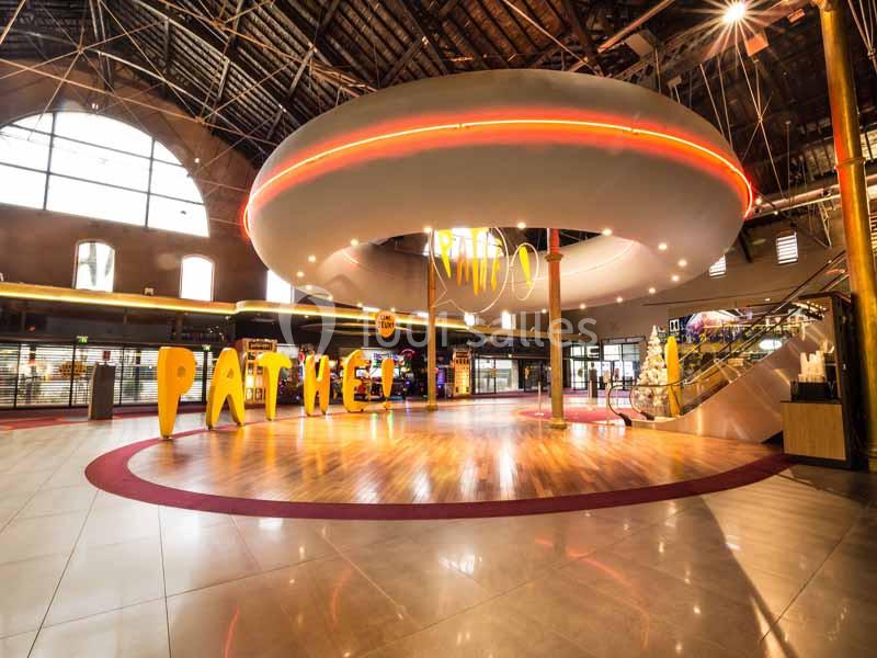 Hall d'entrée lumineux d'un cinéma avec enseigne ’Pathé’, escalier et décorations modernes sous un plafond voûté.