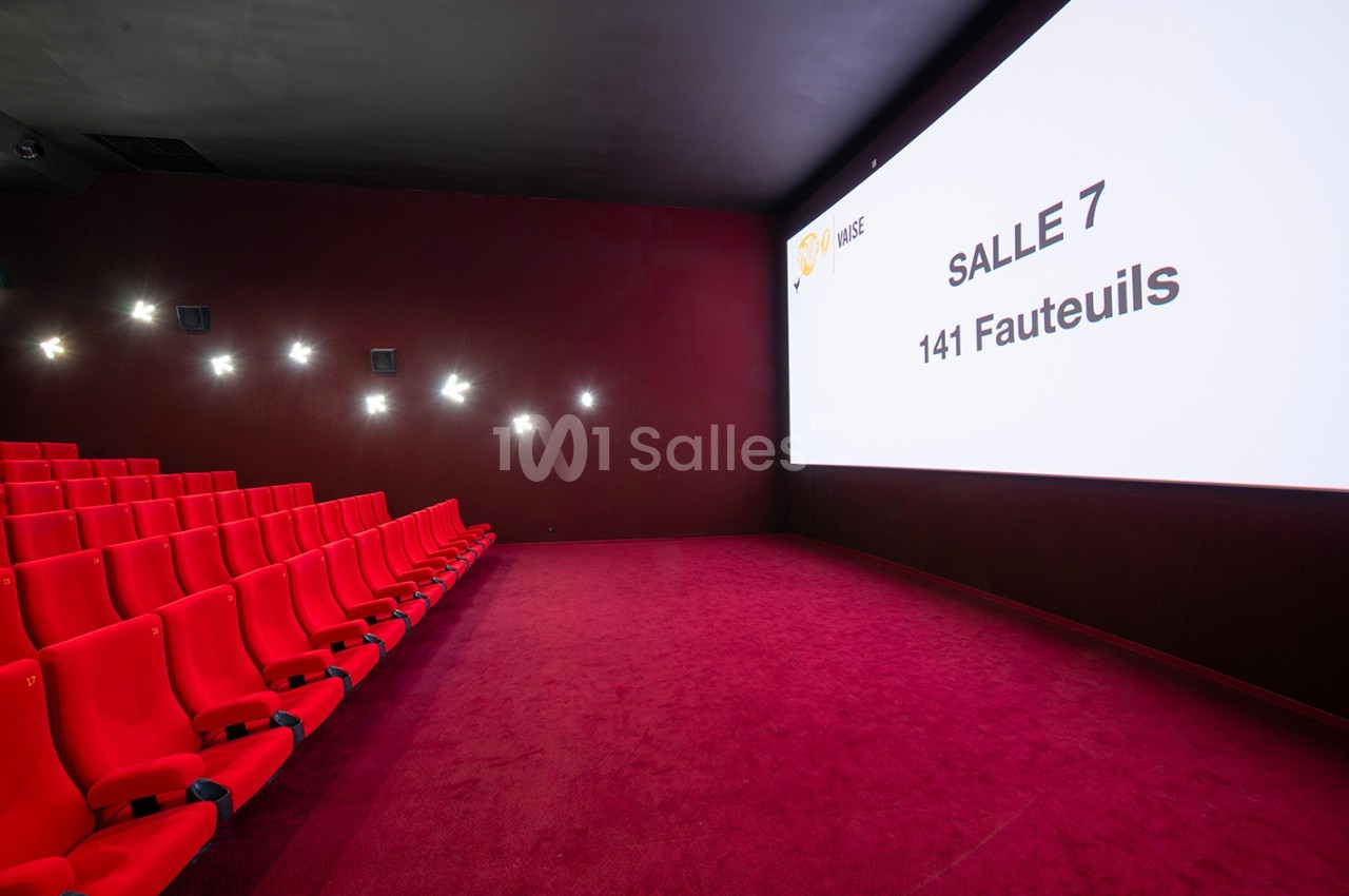 Salle de cinéma vide avec des sièges rouges, un écran affichant ’Salle 7, 141 fauteuils’ et un sol recouvert de moquette…