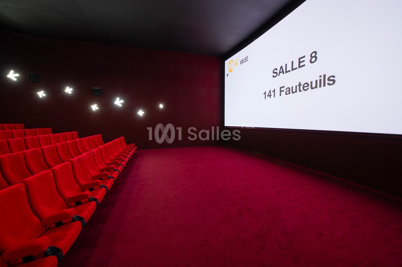 Salle de cinéma vide avec des sièges rouges, écran affichant ’Salle 8, 141 fauteuils’ et éclairage mural discret.