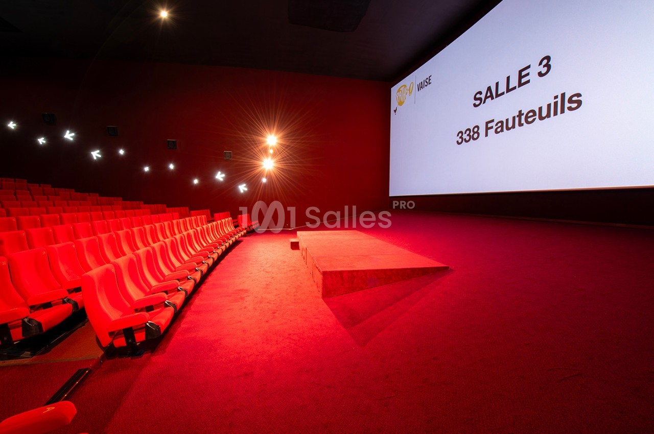 Salle de cinéma vide avec des sièges rouges, un écran affichant ’Salle 3, 338 fauteuils’ et un éclairage tamisé.