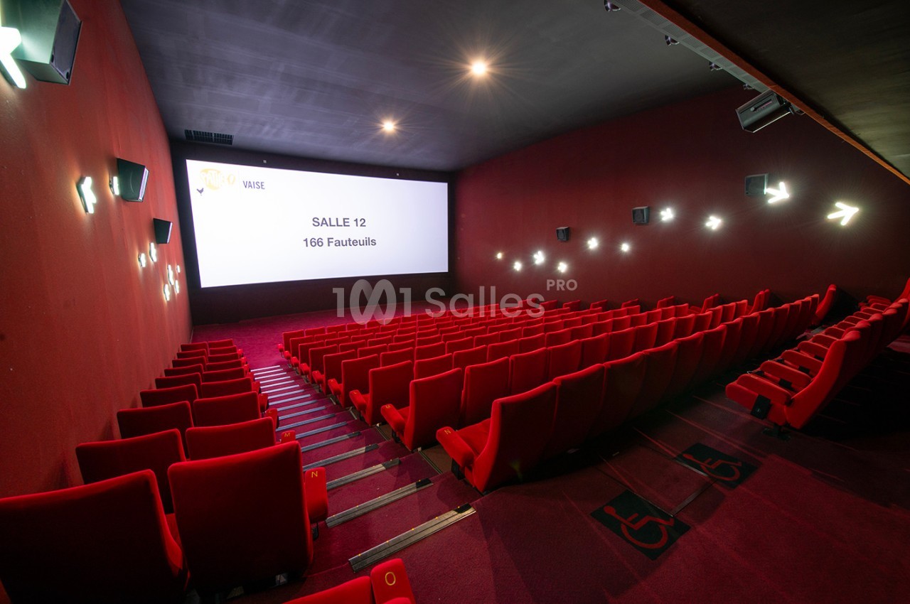 Salle de cinéma vide avec des rangées de fauteuils rouges, écran blanc et éclairage tamisé.
