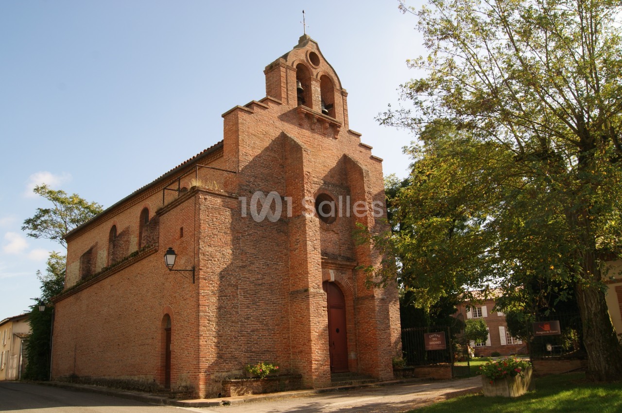 Église en briques rouges avec clocher-mur, entourée d'arbres et située dans un environnement rural.