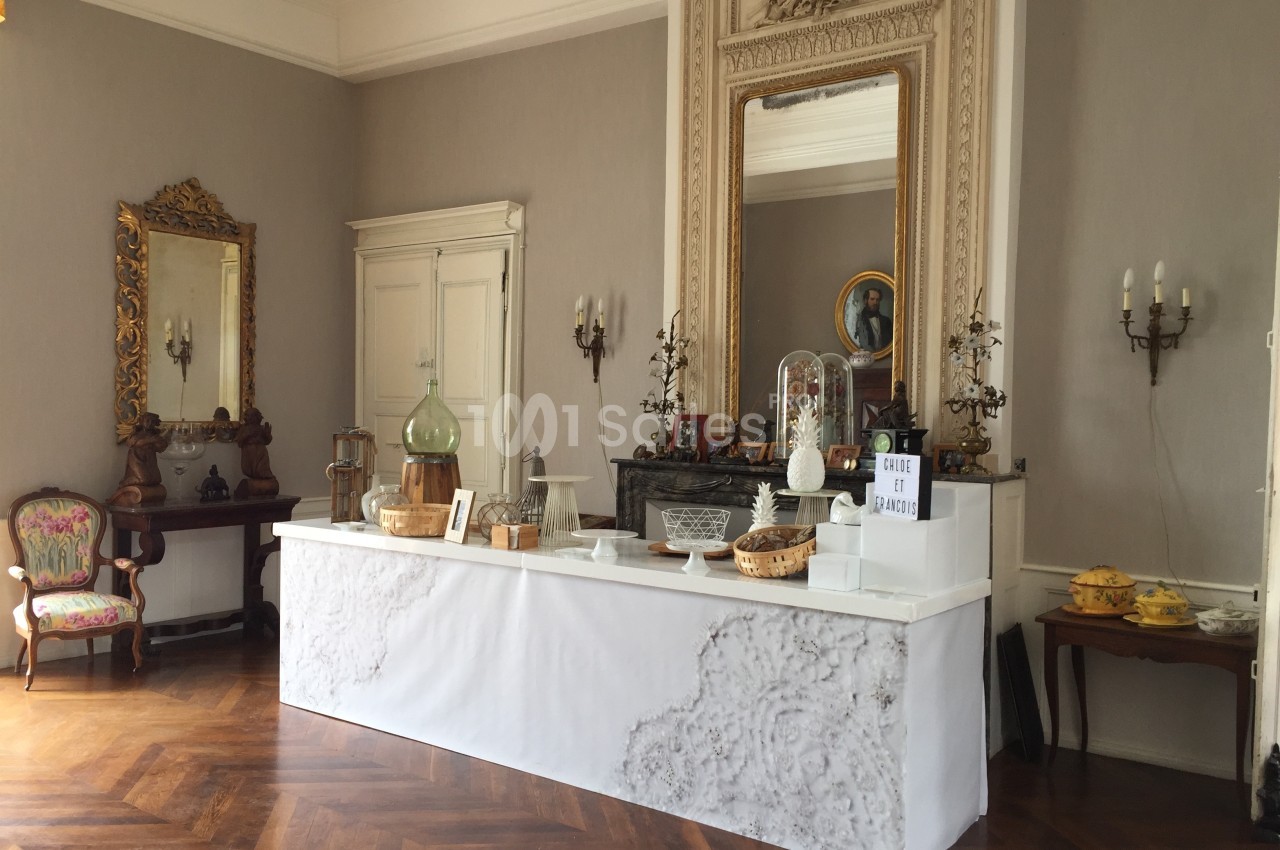 Table de présentation dans une pièce élégante avec parquet, miroirs, chandeliers et objets décoratifs.