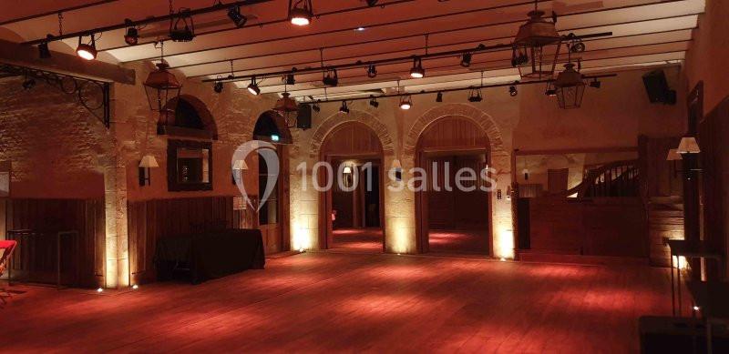 Salle vide avec murs en pierre, parquet en bois, éclairage tamisé et lanternes suspendues.