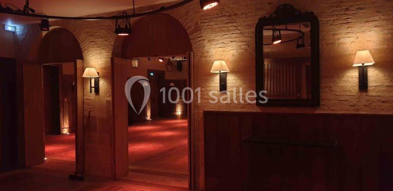 Salle intérieure avec murs en pierre, éclairage tamisé, miroirs et appliques murales diffusant une lumière chaude.