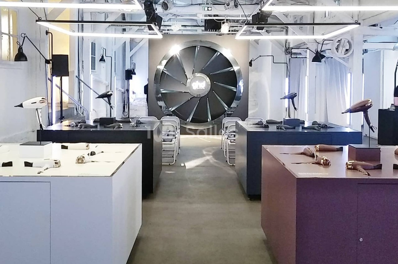 Salle d'exposition moderne avec des meubles et objets design, éclairée par une lumière naturelle et artificielle.