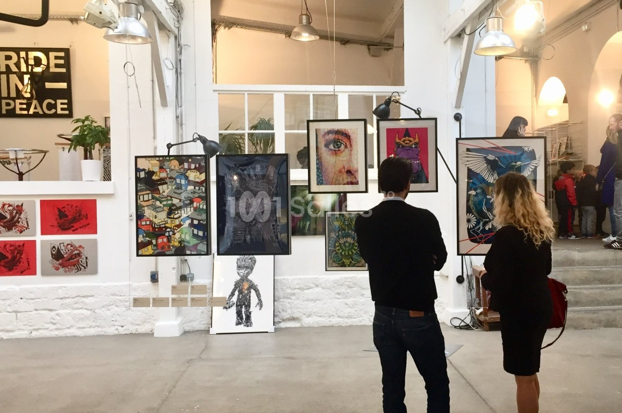 Deux personnes observent des œuvres d'art exposées sur un mur dans une galerie lumineuse au style industriel.