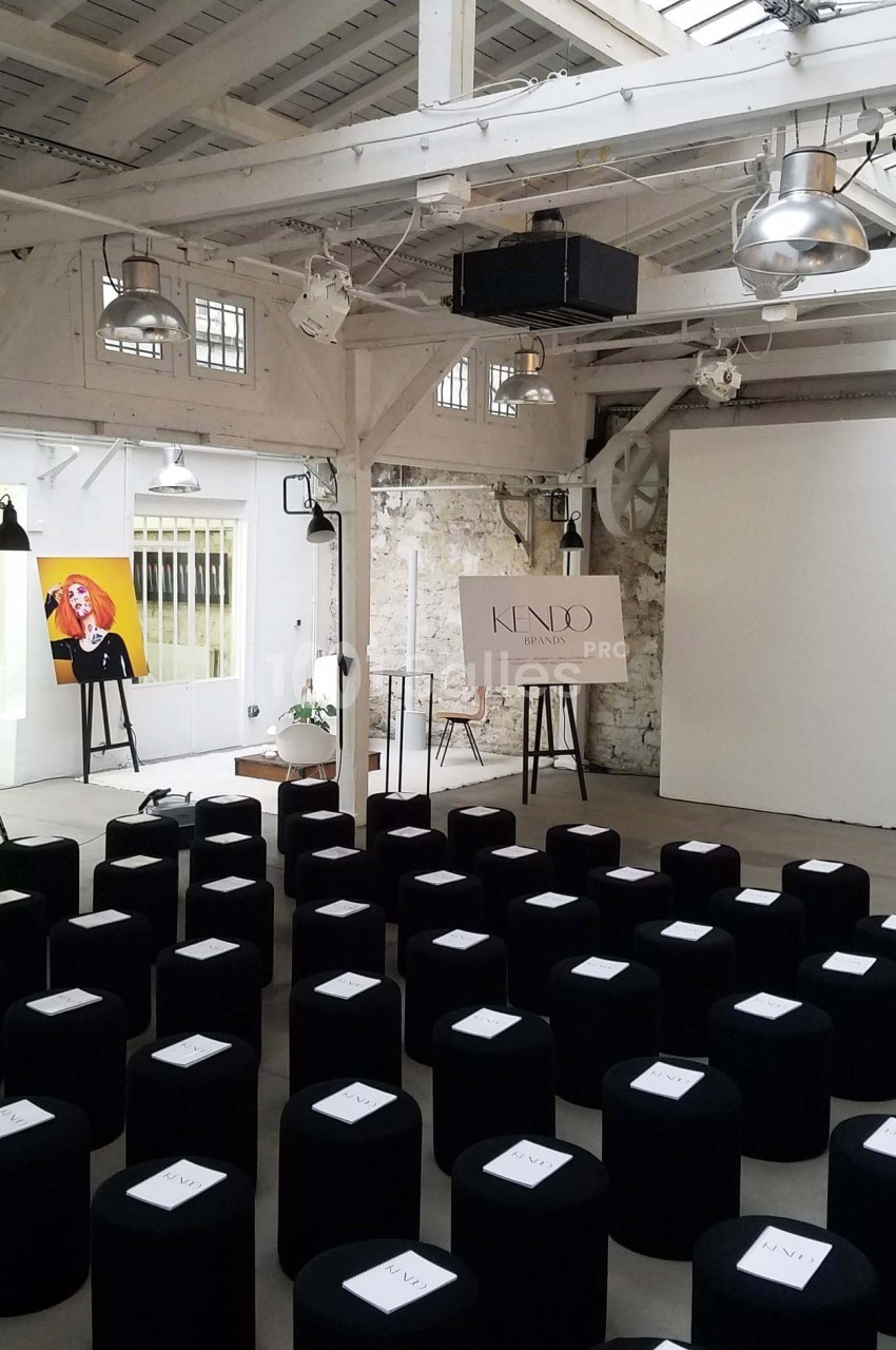 Salle lumineuse avec des sièges noirs alignés, un écran blanc et un chevalet portant une affiche ’Kendo’.