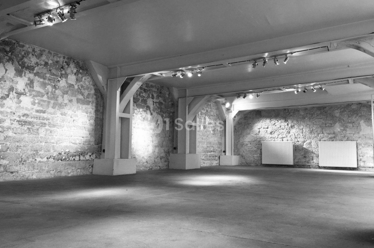 Salle vide avec murs en pierre apparente, poutres en bois et éclairage au plafond.