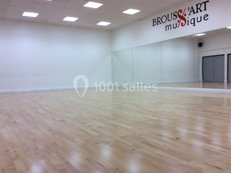 Salle lumineuse avec parquet en bois clair, murs blancs, miroirs sur un côté et logo ’Brouss'Art Musique’ sur le mur.