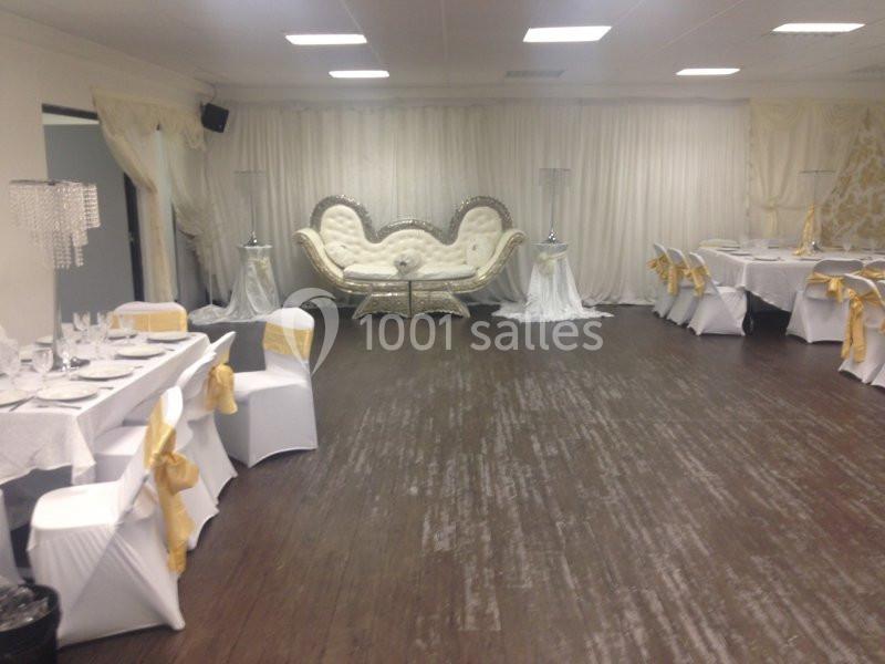 Salle de réception décorée avec des tables blanches ornées de nœuds jaunes et un canapé capitonné au fond.