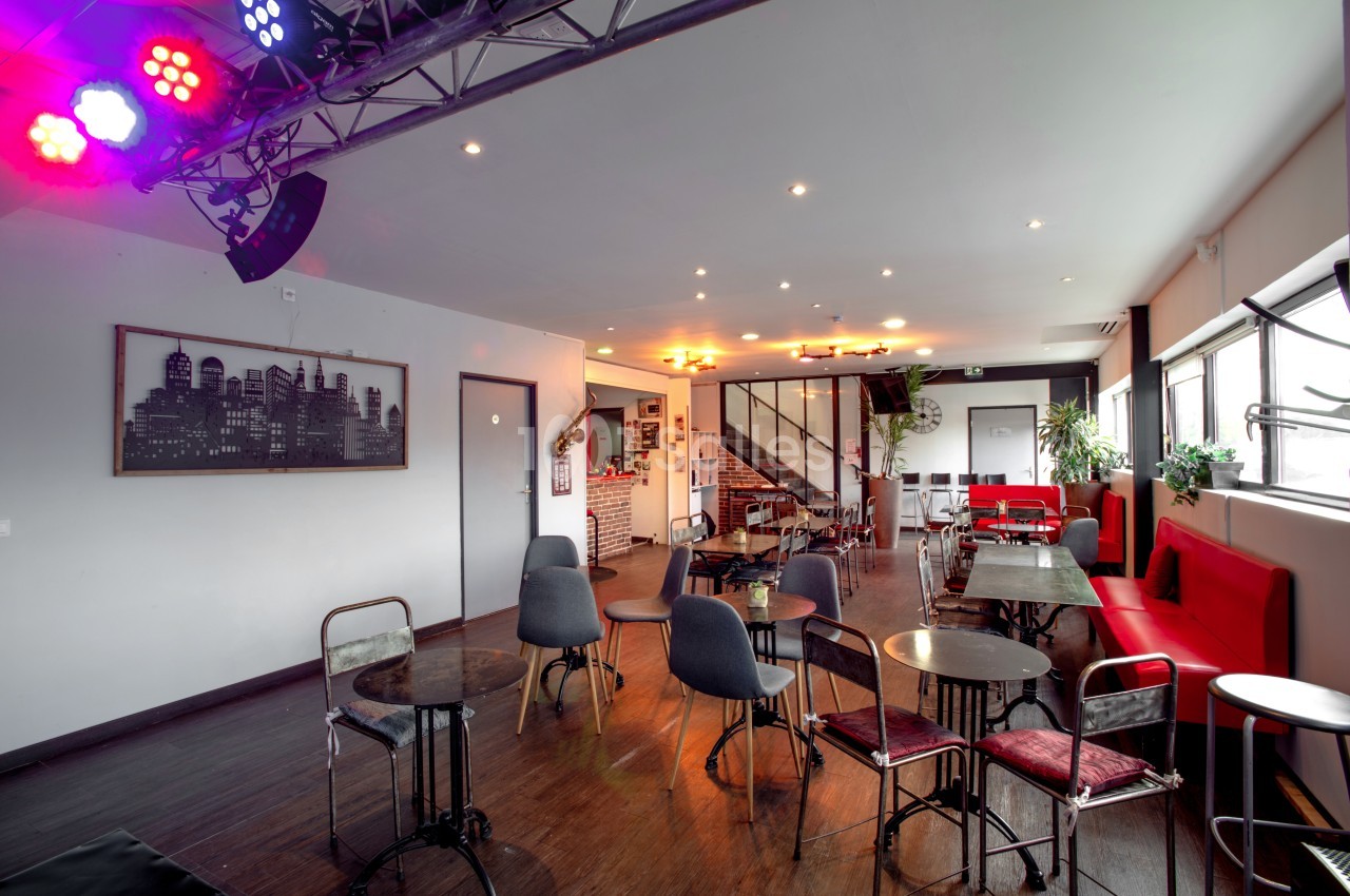 Salle lumineuse avec tables, chaises variées, banquettes rouges, éclairage coloré et décor urbain sur les murs.
