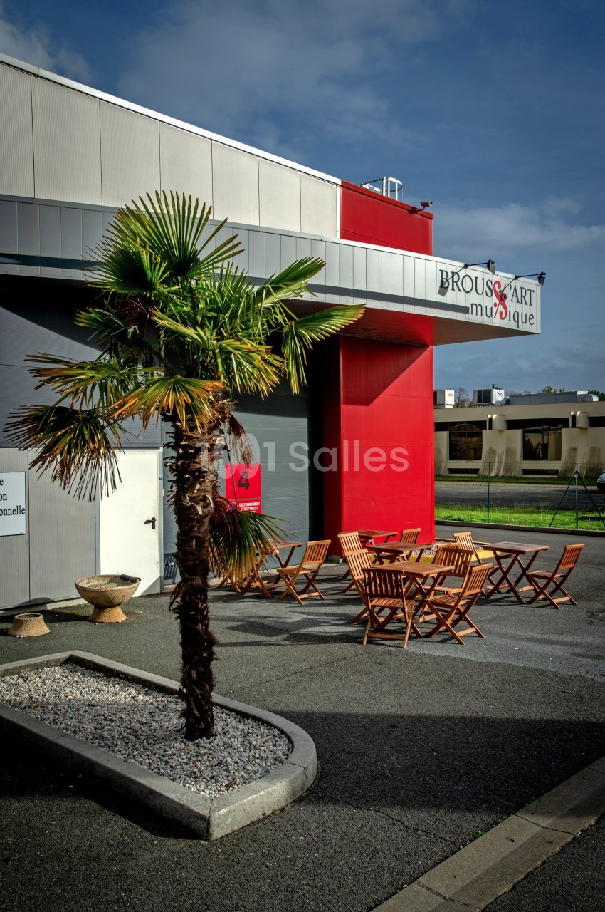 Façade d'un bâtiment avec une enseigne ’Brouss'Art Musique’, terrasse aménagée avec des tables et chaises en bois.