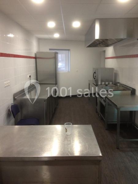 Cuisine professionnelle équipée avec plans de travail en inox, four, plaque de cuisson et hotte, éclairée par des spots au…
