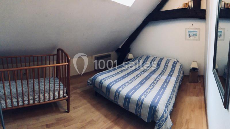 Chambre mansardée avec un lit double, un lit bébé en bois, parquet au sol et poutres apparentes.