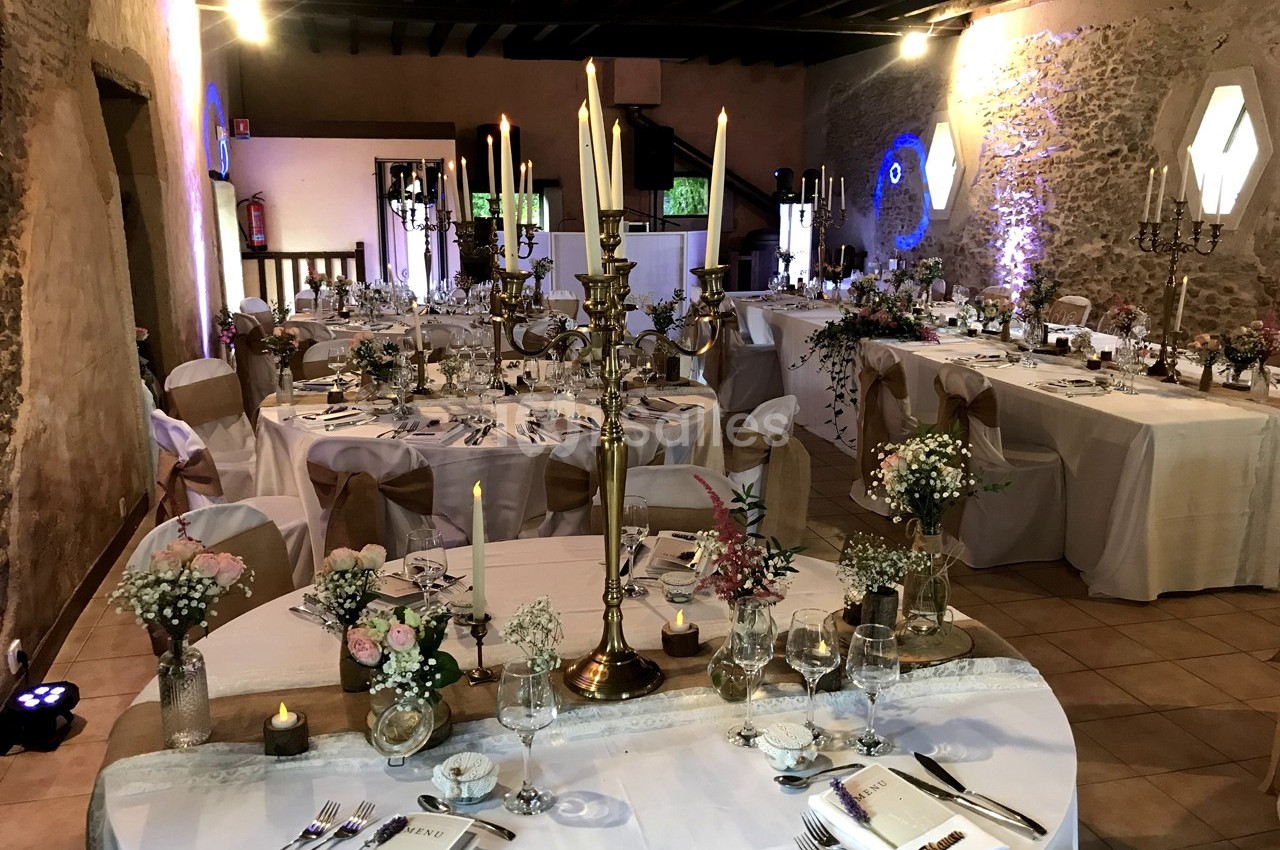 Salle de réception décorée pour un mariage avec tables rondes et rectangulaires ornées de chandeliers et fleurs.