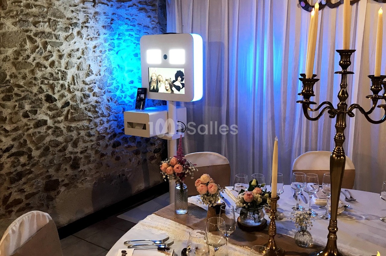 Borne photo lumineuse installée dans une salle de réception, entourée de décorations florales et d'une table dressée.