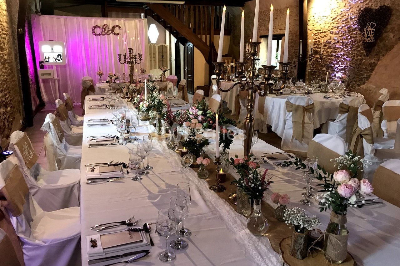 Salle de réception décorée pour un mariage avec tables dressées, chandeliers, fleurs et éclairage tamisé.