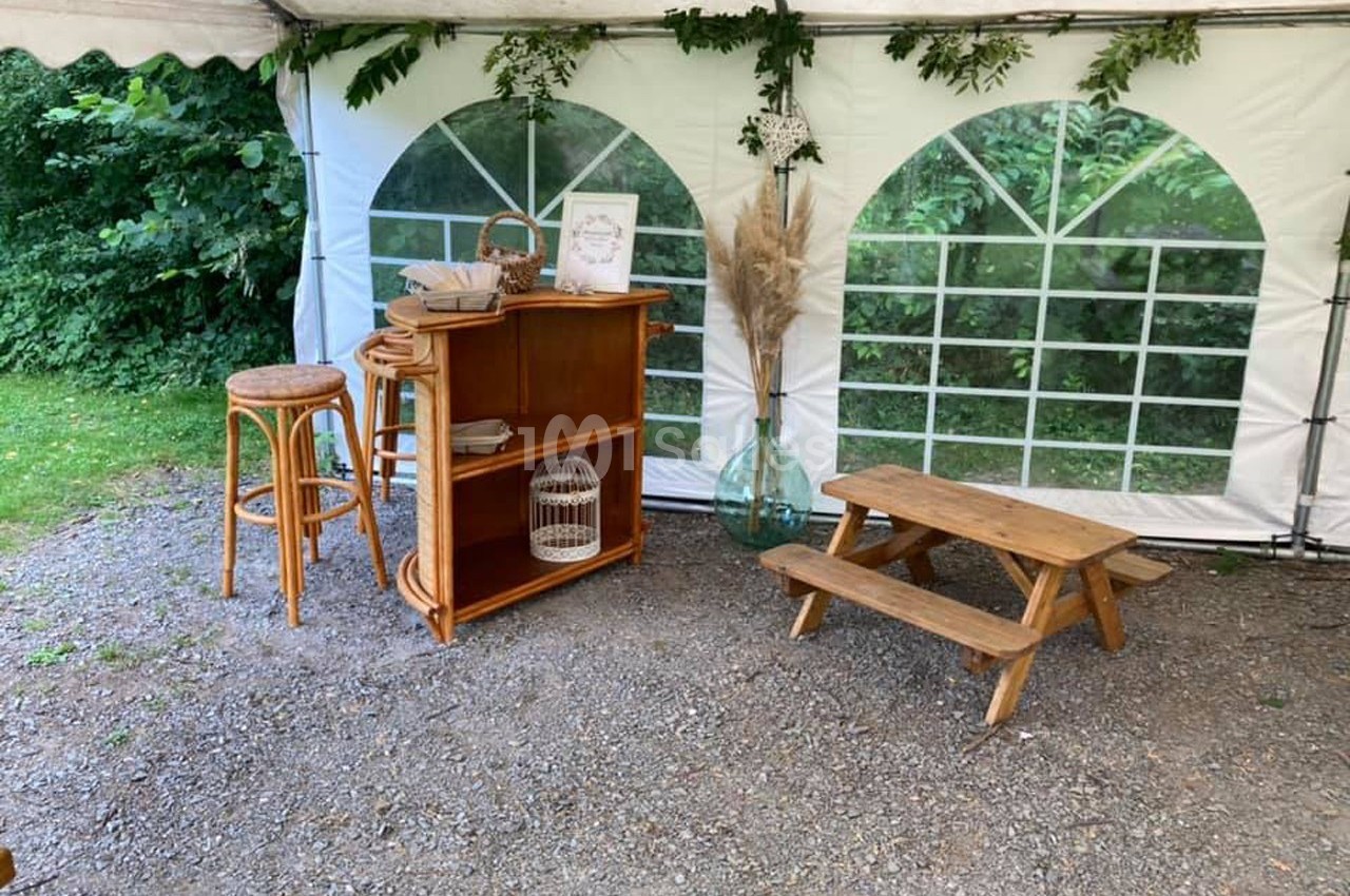 Un coin aménagé sous une tente avec un comptoir en bois, des tabourets, une table basse et des éléments décoratifs naturels.