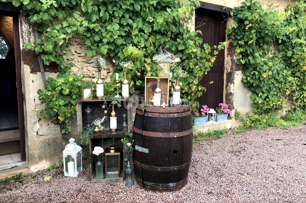 Décoration rustique avec tonneau, caisses en bois, bouteilles fleuries et lanternes devant un mur couvert de vigne.