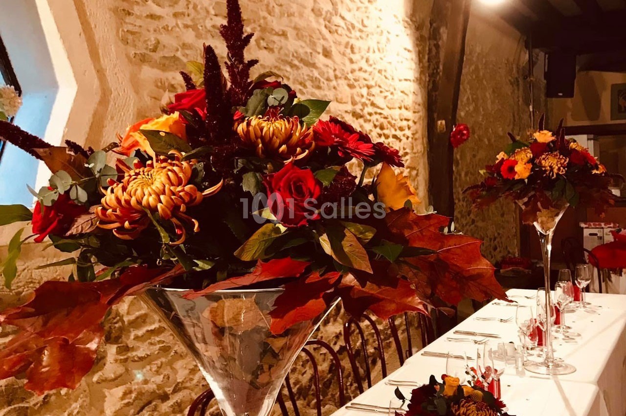 Bouquets de fleurs automnales avec des roses et des feuilles rouges décorant une table dans une salle en pierre.