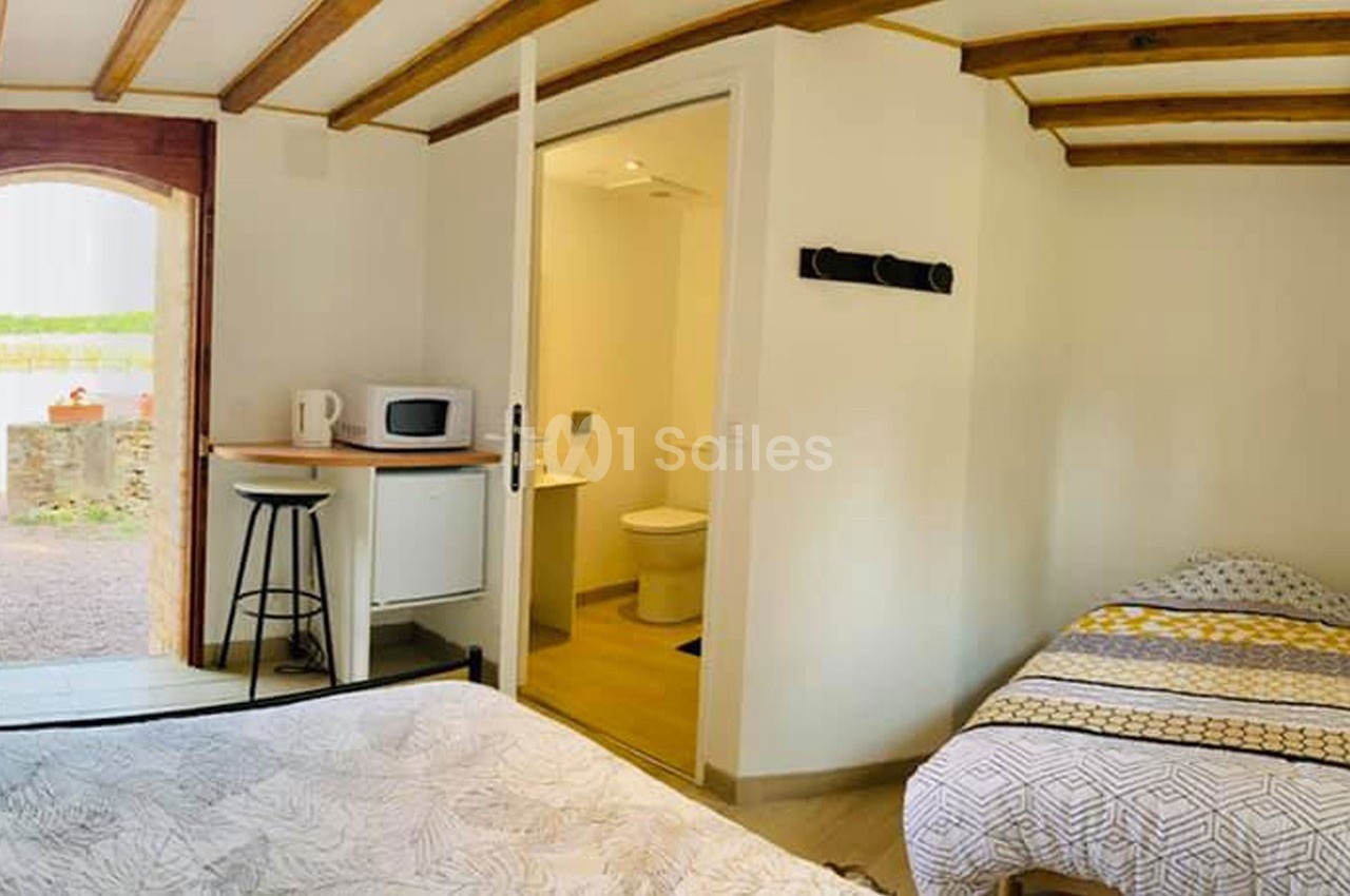 Chambre lumineuse avec deux lits, kitchenette équipée d'un micro-ondes et salle de bain attenante.