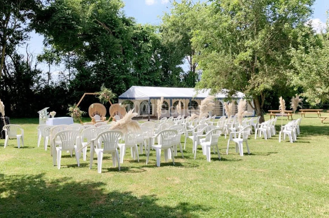 Chaises blanches disposées en rangées sur une pelouse, face à une tente décorée pour un événement en plein air.