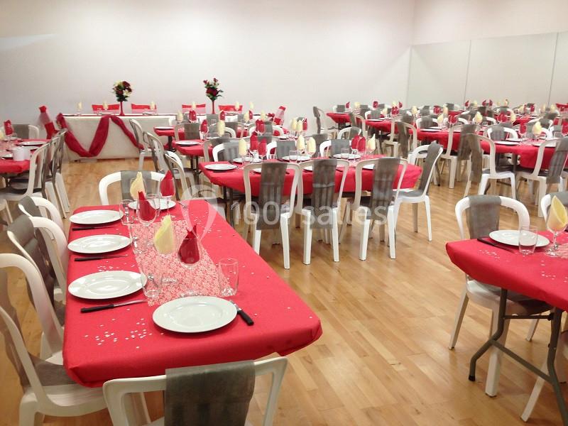 Salle de réception décorée avec des nappes rouges, des chaises blanches et grises, et des tables dressées pour un événement.