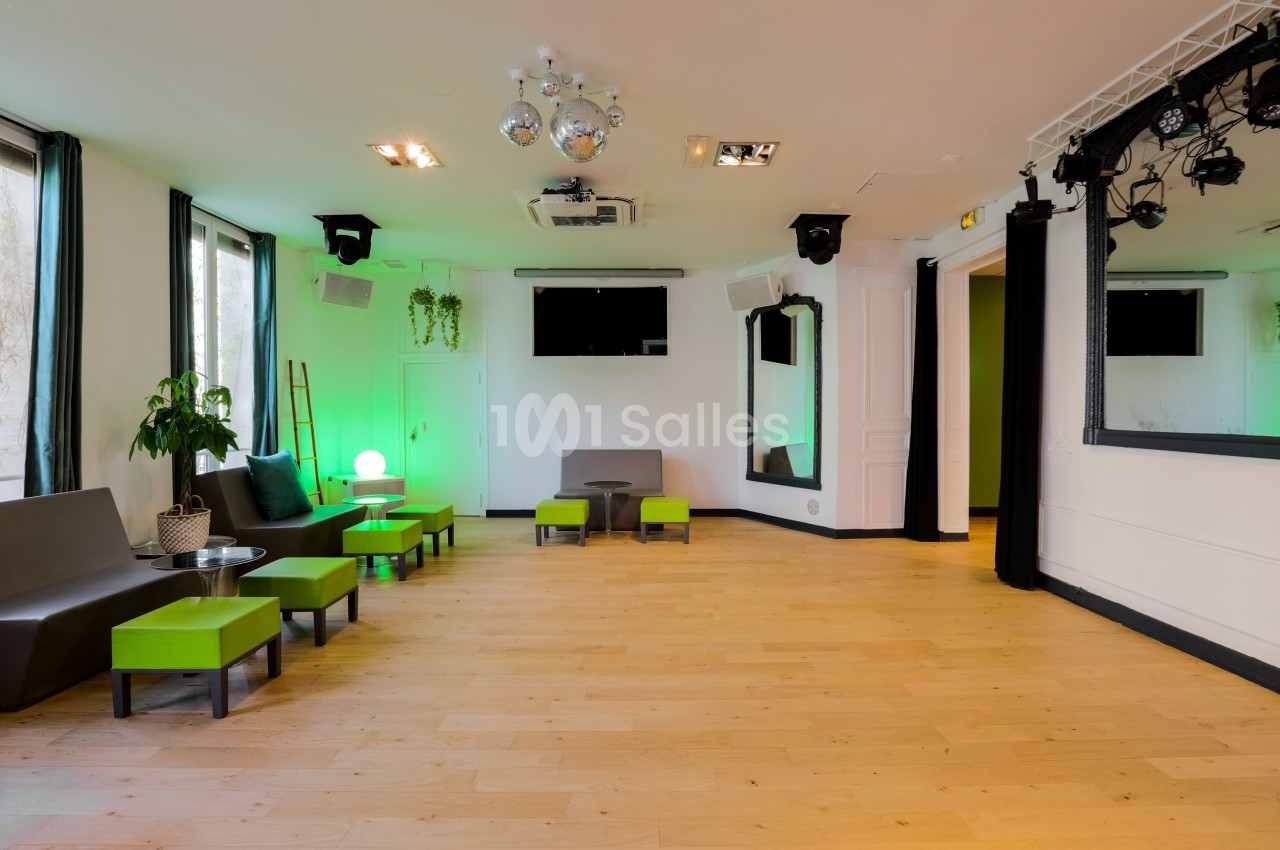 Salle lumineuse avec parquet, mobilier moderne vert et gris, éclairage décoratif et scène équipée de projecteurs.