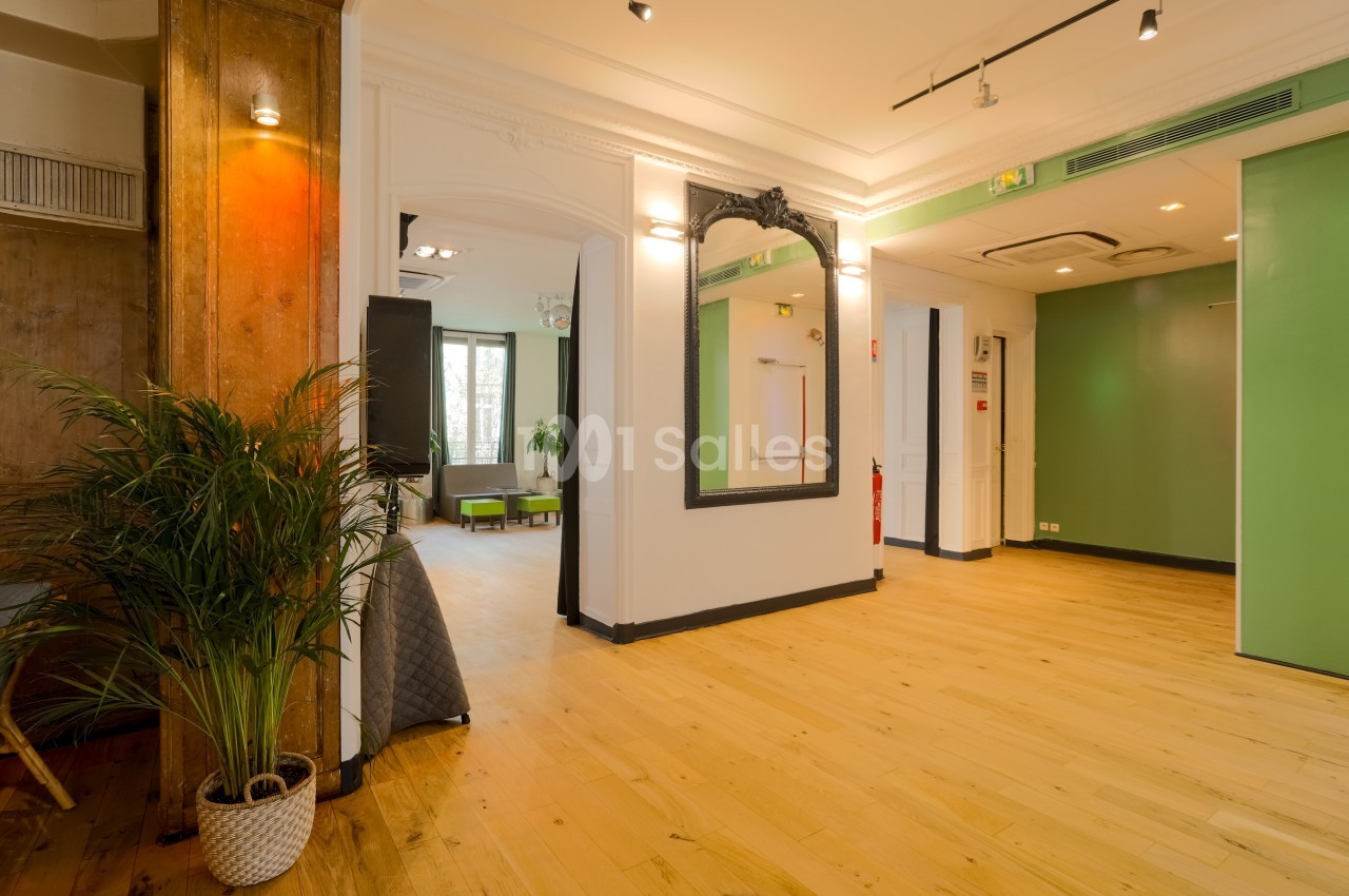 Intérieur lumineux avec parquet, murs blancs, miroir encadré noir, plantes et portes vertes.