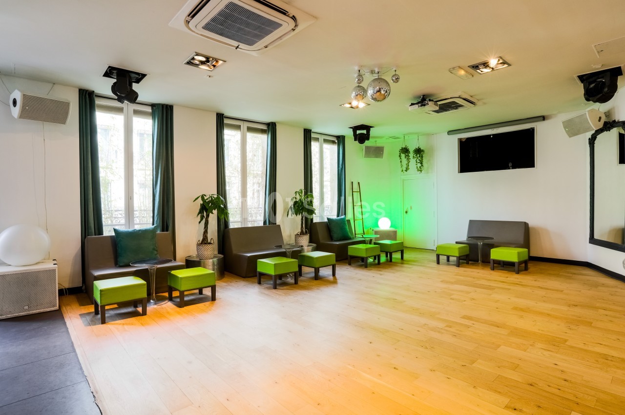 Salle lumineuse avec parquet, fauteuils gris et verts, plantes, miroirs, éclairage moderne et fenêtres donnant sur l…