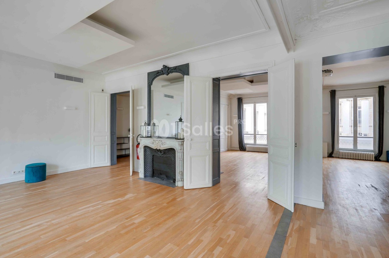 Salon lumineux avec parquet en bois clair, cheminée décorative, moulures au plafond et grandes fenêtres.