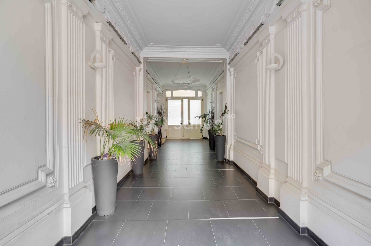 Couloir lumineux avec carrelage sombre, moulures décoratives blanches et plantes en pots près des murs.