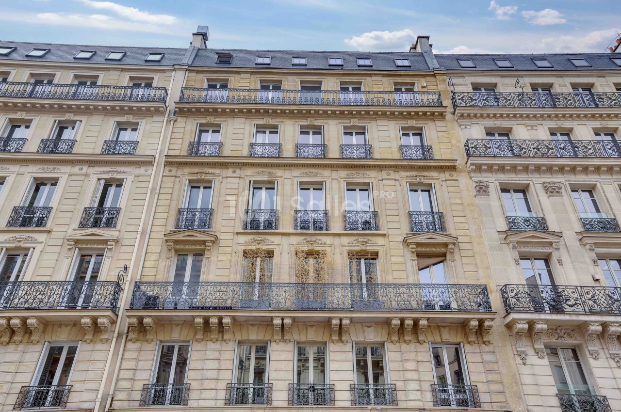 Façade d'un immeuble haussmannien avec balcons en fer forgé et fenêtres alignées sur plusieurs étages.