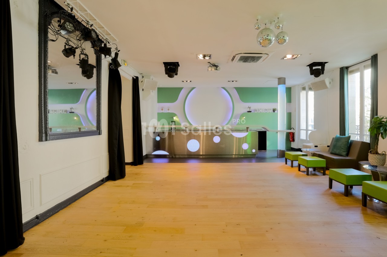 Salle lumineuse avec parquet, comptoir moderne éclairé, sièges verts et grandes fenêtres laissant entrer la lumière…