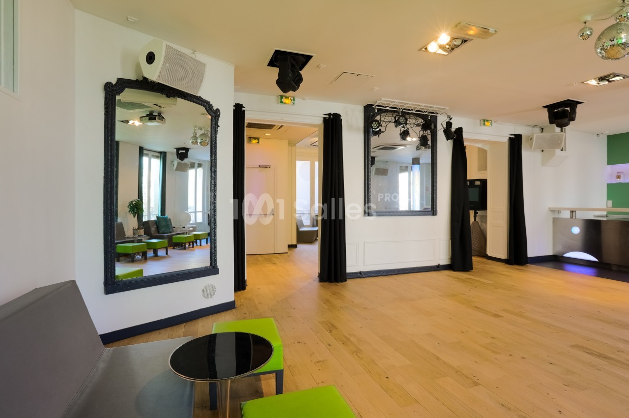 Salle lumineuse avec parquet clair, miroirs encadrés, rideaux noirs, mobilier moderne et éclairage suspendu.