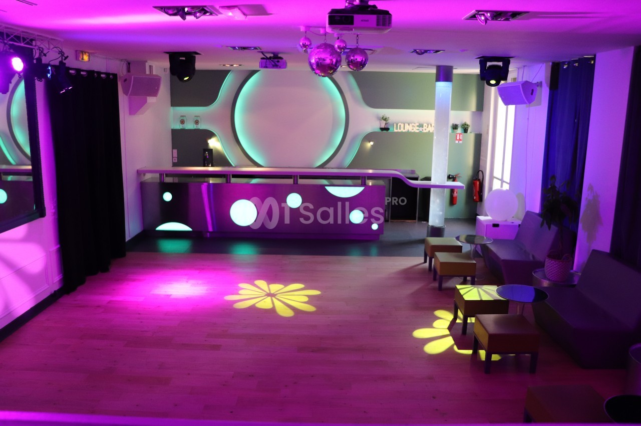 Salle de réception avec piste de danse éclairée par des lumières colorées, bar moderne en arrière-plan.