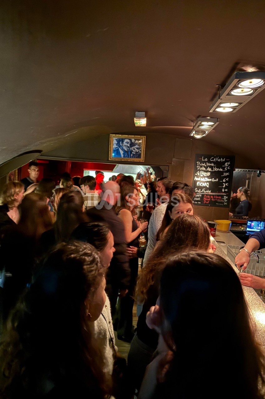 Groupe de personnes discutant et commandant des boissons dans un bar animé avec une ambiance tamisée.