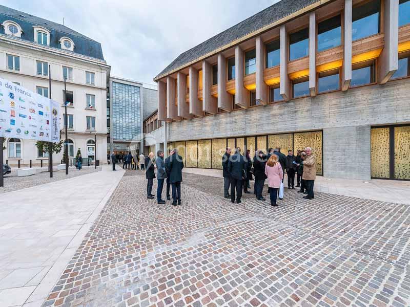 Groupe de personnes discutant sur une place pavée devant des bâtiments modernes et anciens.
