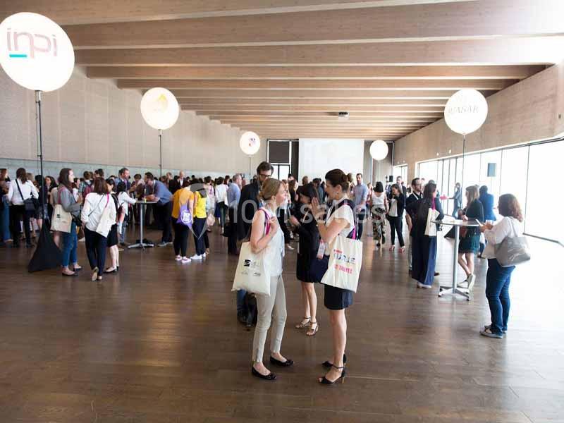 Des personnes échangent et se rassemblent dans une grande salle lumineuse lors d'un événement professionnel.