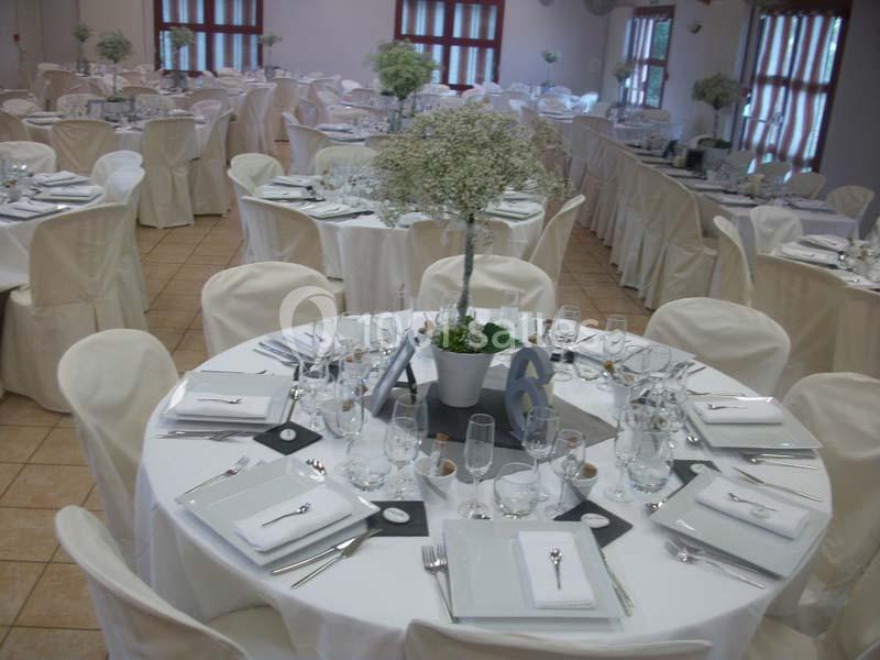 Salle de réception avec tables rondes dressées, nappes blanches, couverts élégants et centres de table fleuris.